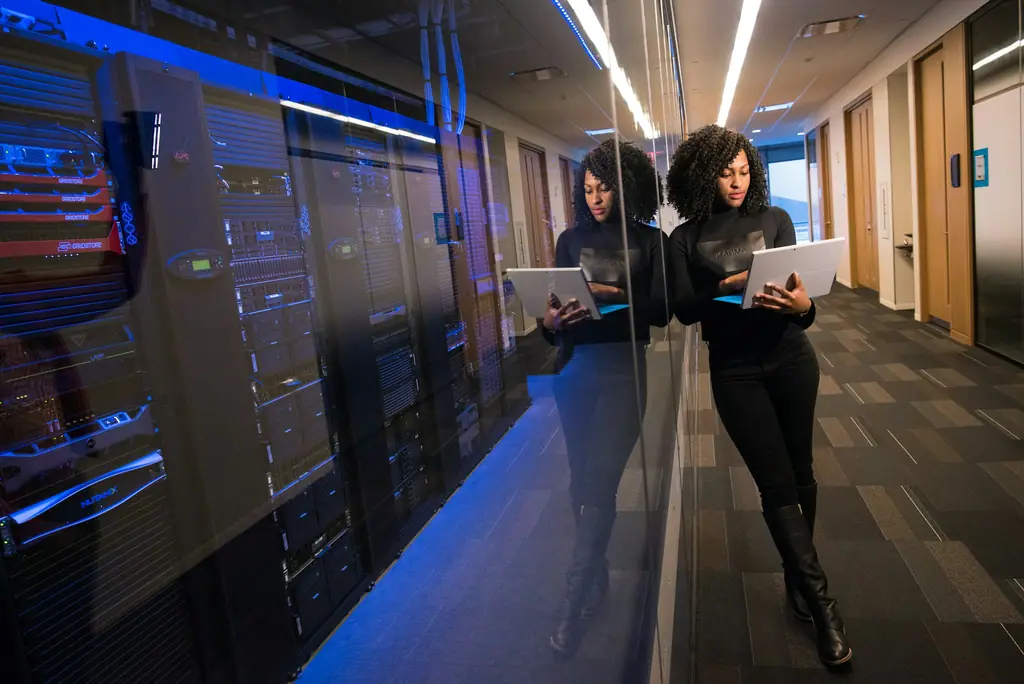 Two people walking with tablets through a brightly lit server room corridor
