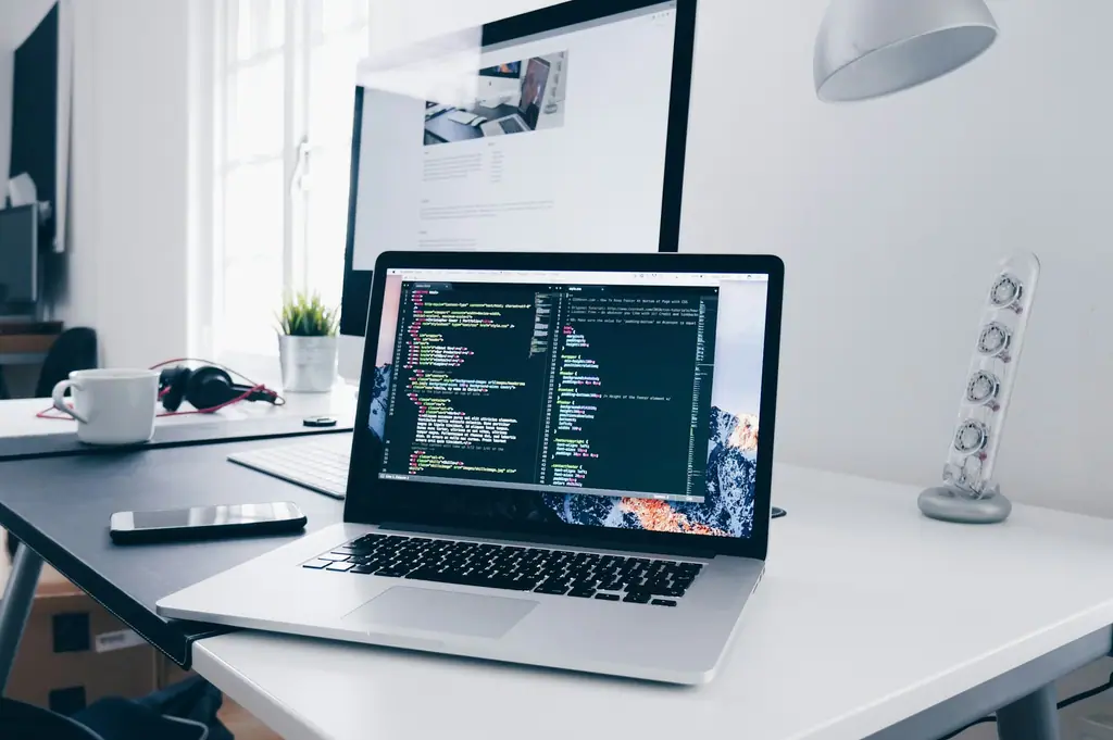 A clean desk with a laptop displaying code beside a coffee cup and a small plant