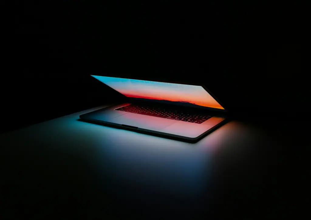 A partially open laptop glowing with orange and blue light in a dark room