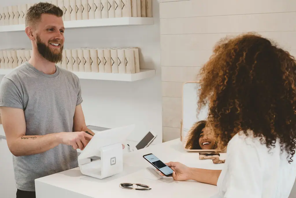 A shop assistant smiling while a customer pays by phone at a modern retail counter