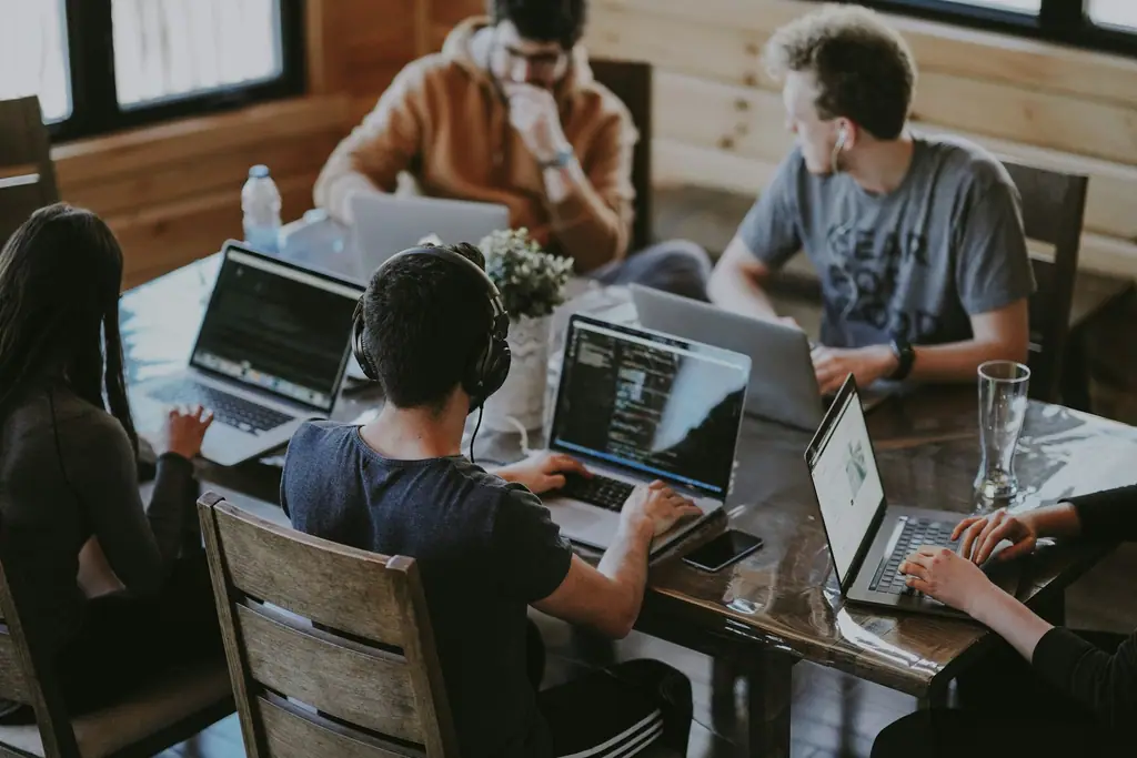 A small team working together around a wooden table with laptops and notebooks